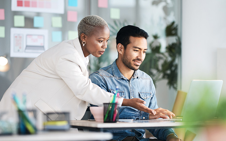 A woman and man in an office collaborating while looking at a laptop screen.