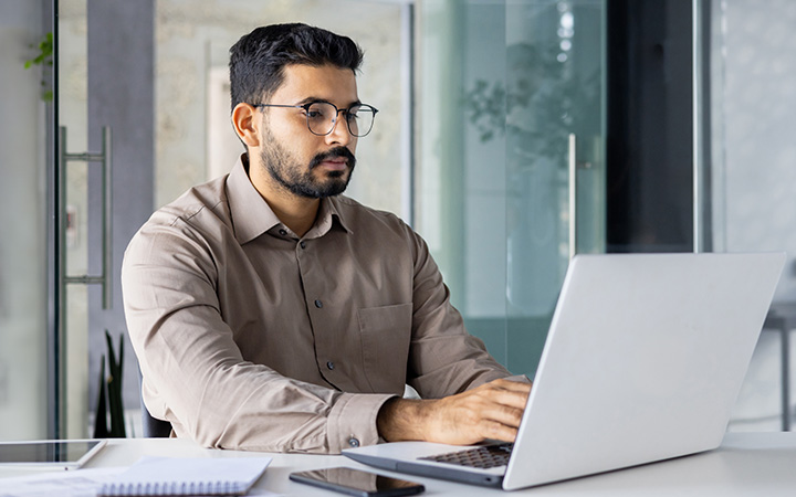 A man seated at a desk in an office working on a laptop.