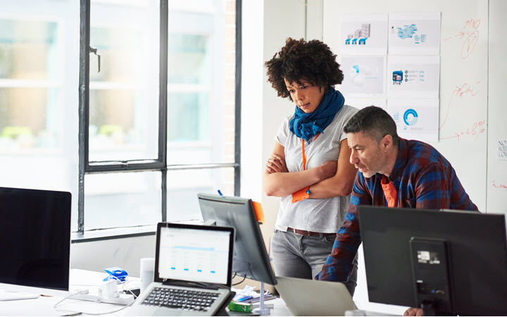 A woman and a man in an office, standing, looking at a computer monitor.